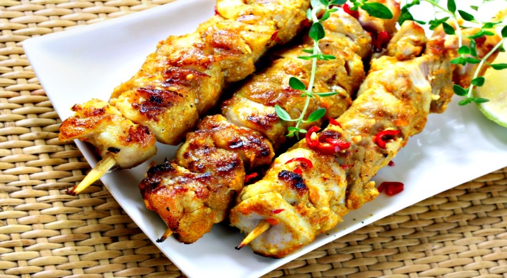 Skewers of grilled chicken with red chili, thyme, and lime wedges.