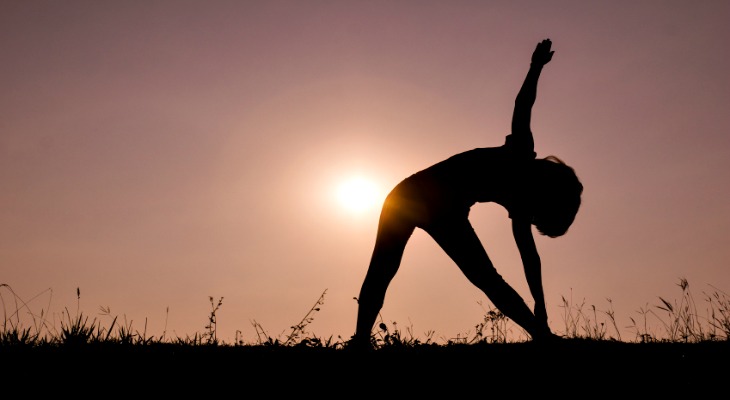 Triangle pose yoga with young woman silhouette on sunset sky.